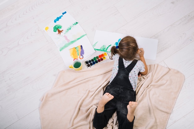 Photo gratuite fille qui peint à l'aquarelle sur du papier et se trouvant sur le sol