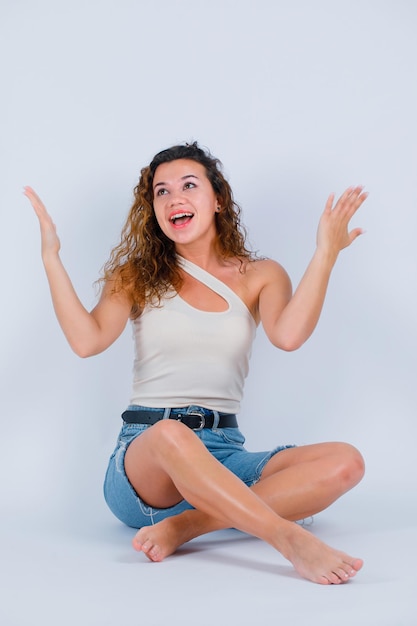 La fille qui rit regarde en levant les mains sur fond blanc