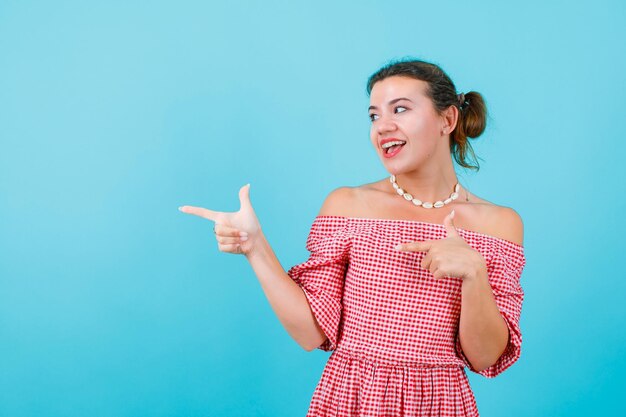 La fille qui rit regarde et pointe vers la gauche avec des avant-bras sur fond bleu