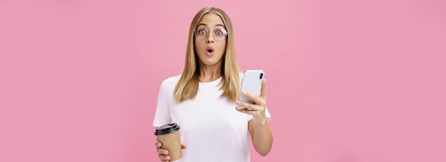 Photo gratuite une fille reçoit un message génial sur son smartphone tout en buvant du café dans une tasse dans un café partageant des nouvelles