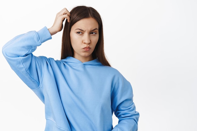 Fille réfléchie confuse, gratter la tête et regarder de côté perplexe, penser à quelque chose, plisser les yeux et regarder à gauche, debout sur fond blanc