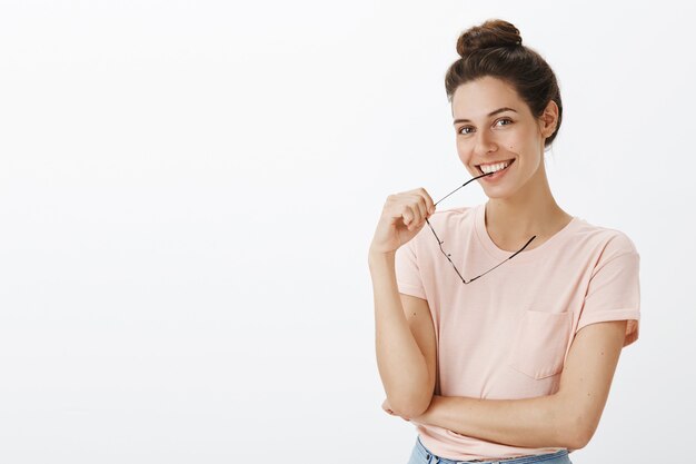 Fille réfléchie incertaine avec des lunettes posant contre le mur blanc