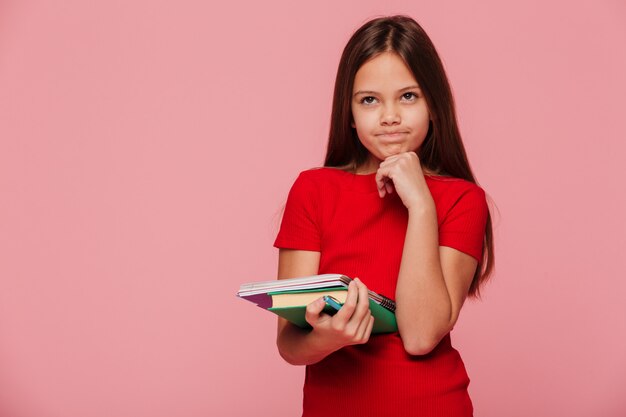 Fille réfléchie en robe rouge tenant le livre et à la recherche