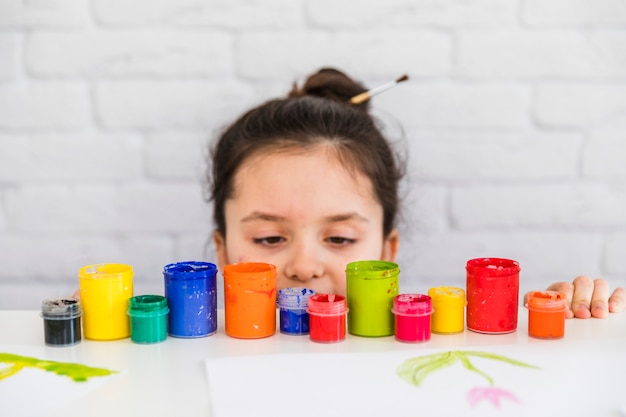 Fille regardant des bouteilles de peinture colorée au bord d&#39;une table blanche