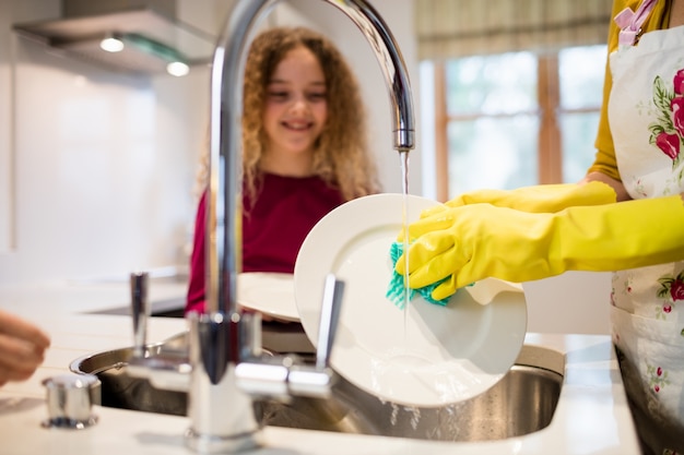 Fille regardant la mère tout en lavant la plaque dans la cuisine