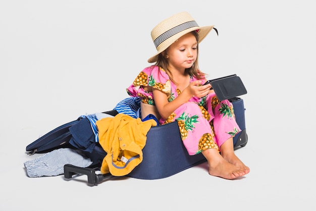 Photo gratuite fille regardant une tablette assise sur une valise
