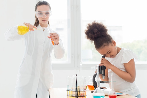 Fille regardant à travers le microscope avec femme scientifique et potions