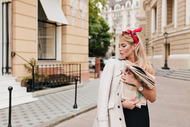 Une fille rêveuse aux cheveux blonds courts a acheté des journaux et rentre à la maison pour les lire