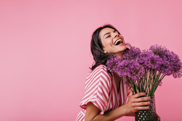 Fille en robe d'été rose apprécie le parfum des fleurs et rit sincèrement, profitant d'une excellente journée de printemps.