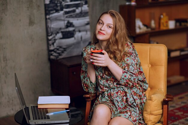 Fille en robe à fleurs assise et tenant une tasse de café marron.