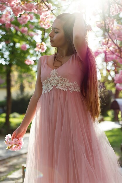 Fille en robe rose se tient sous la floraison des arbres de sakura dans le parc