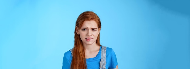 Photo gratuite fille rousse bouleversée mal à l'aise se sentir mal à l'aise regard frustré mordant la lèvre fronçant les sourcils tirer vers le haut du visage triste