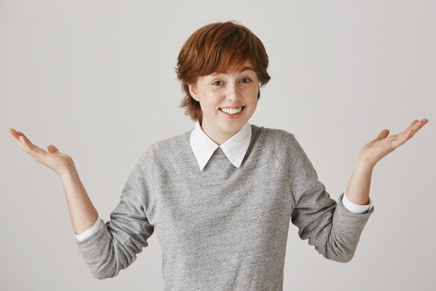 Fille rousse confuse et indifférente avec une coupe courte posant contre le mur blanc