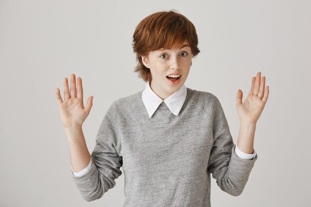 Fille rousse désemparée et confuse avec une coupe de cheveux courte posant contre le mur blanc