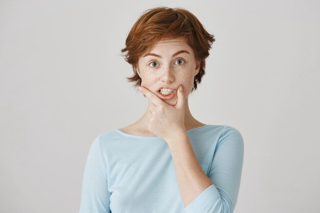 Fille rousse drôle posant contre le mur blanc