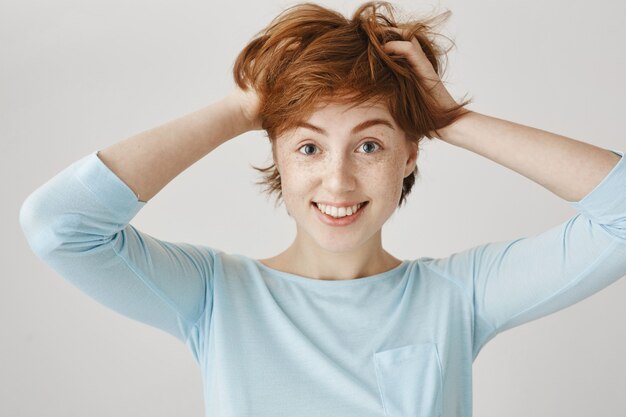 Fille rousse heureuse posant contre le mur blanc