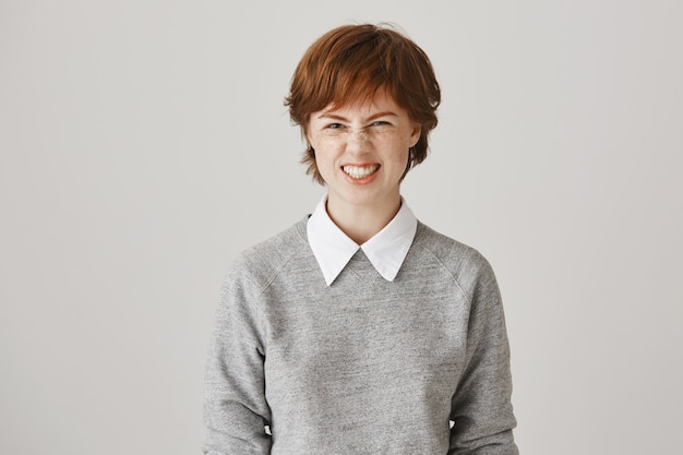 Fille rousse impertinente et insouciante avec une coupe de cheveux courte posant contre le mur blanc