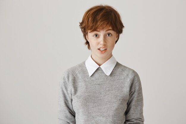 Fille rousse incertaine avec une coupe de cheveux courte posant contre le mur blanc