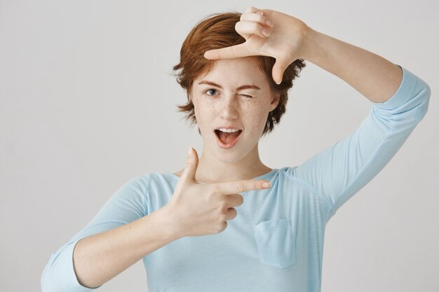 Fille rousse insouciante posant contre le mur blanc