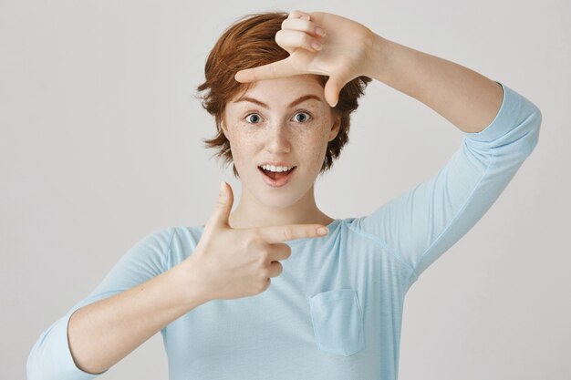 Fille rousse insouciante posant contre le mur blanc