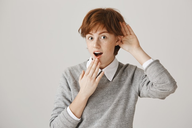 Fille rousse intriguée avec coupe de cheveux courte posant contre le mur blanc