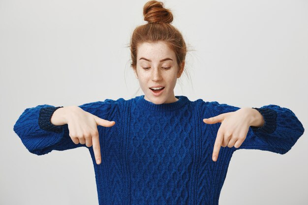 Fille rousse intriguée pointant les doigts vers le bas