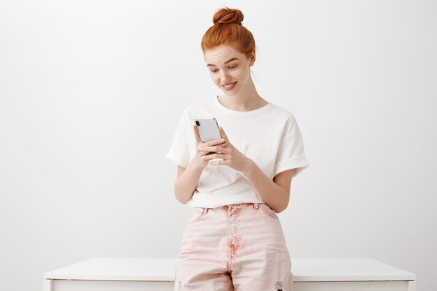 Fille rousse intriguée regardant un téléphone mobile intéressé