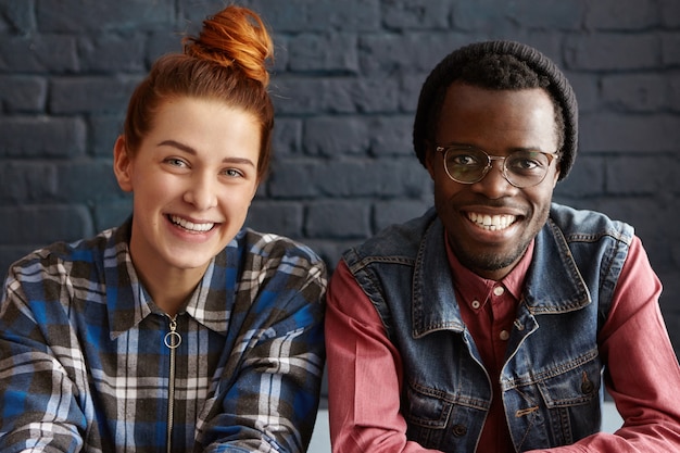 Photo gratuite fille rousse joyeuse avec beau sourire assis près de son beau petit ami dans un chapeau élégant et des lunettes