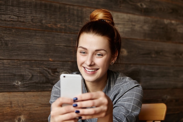 Photo gratuite fille rousse joyeuse avec chignon lecture sms sur téléphone portable générique