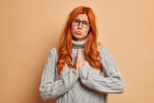 La fille rousse mendiant bouleversée garde les paumes pressées l'une contre l'autre implore la pitié fait le geste de prière a pitié l'expression demande quelque chose en utilisant le langage corporel.