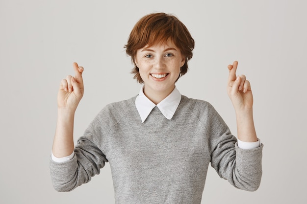 Fille rousse pleine d'espoir avec une coupe de cheveux courte posant contre le mur blanc