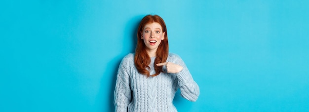 Photo gratuite fille rousse pleine d'espoir pointant vers elle-même debout sur fond bleu