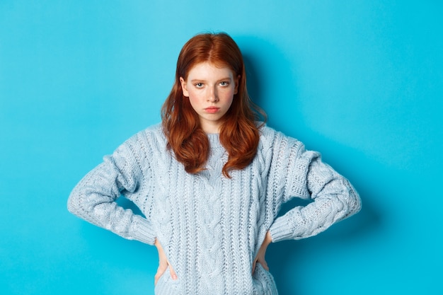 Fille Rousse Regardant En Colère Et Mécontente De La Caméra, Fronçant Les Sourcils Contrarié, Debout Sur Fond Bleu.