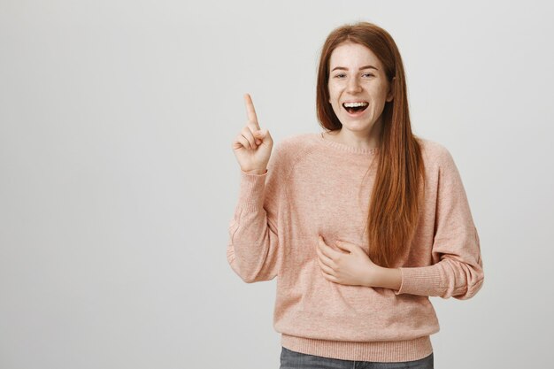 Fille rousse riante heureuse pointant vers le haut et gloussant