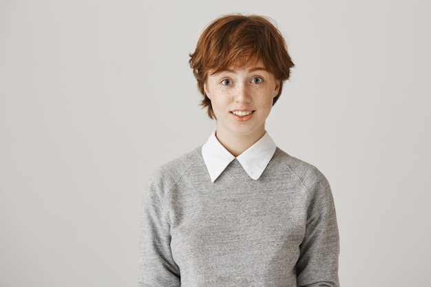 Fille rousse surprise avec coupe de cheveux courte posant contre le mur blanc