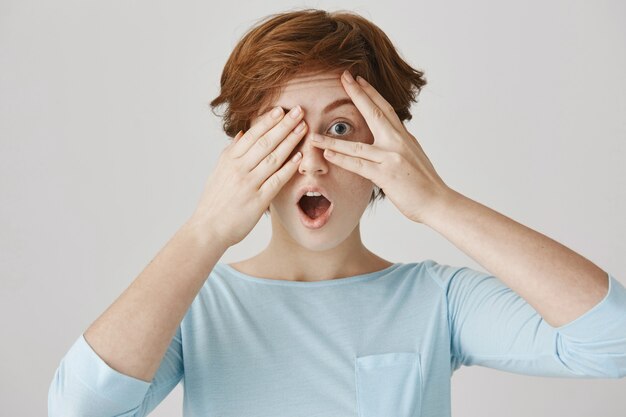 Fille rousse surprise posant contre le mur blanc