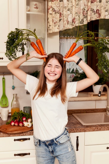 Photo gratuite fille s'amusant avec des carottes dans la cuisine