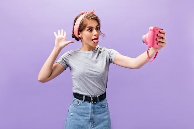 Fille s'amusant, prend selfie sur fond violet. Drôle jeune femme de bonne humeur en chemise grise et jupe en jean sur fond violet.