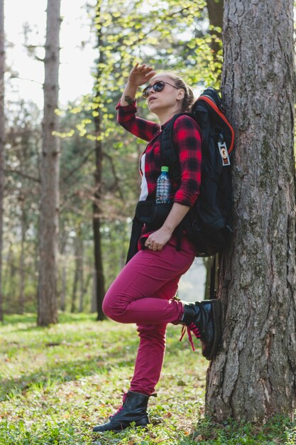 Fille avec un sac à dos appuyé contre un arbre