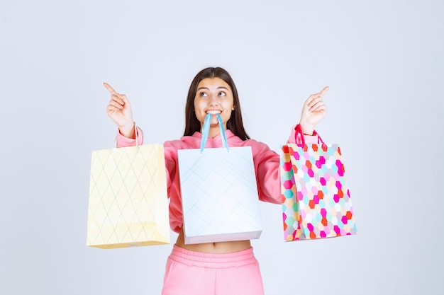 Fille avec des sacs colorés les tenant dans les mains et la bouche.