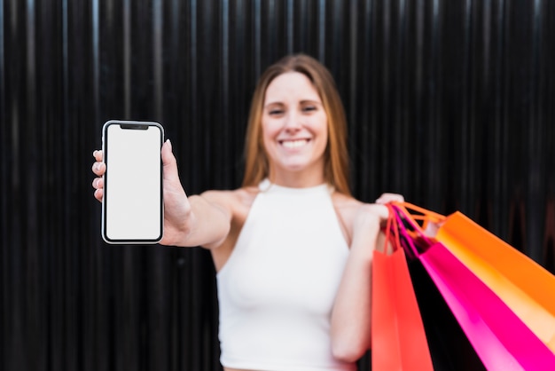 Fille avec des sacs à provisions tenant une maquette de téléphone