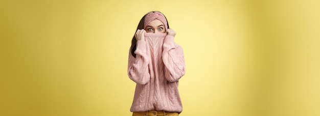 Photo gratuite fille se cachant dans le col portant un chandail tricoté sur le nez qui saute les yeux regardant les yeux sur écoute à l'appareil photo h