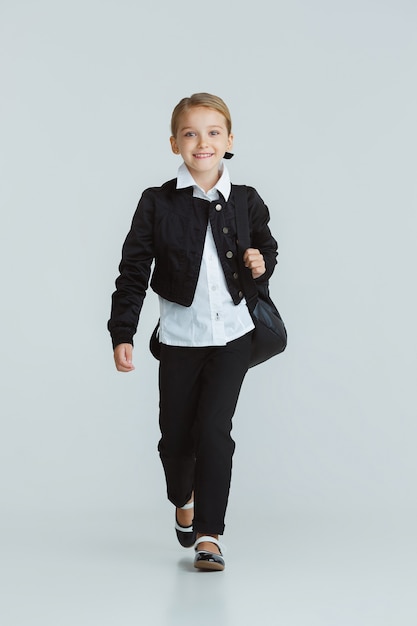 Fille se préparant à l'école après une longue pause estivale. Retour à l'école. Petit modèle caucasien féminin posant en uniforme scolaire sur un mur blanc. Enfance, éducation, concept de vacances.