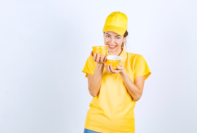 Fille de sexe féminin en uniforme jaune tenant deux tasses de nouilles à emporter.