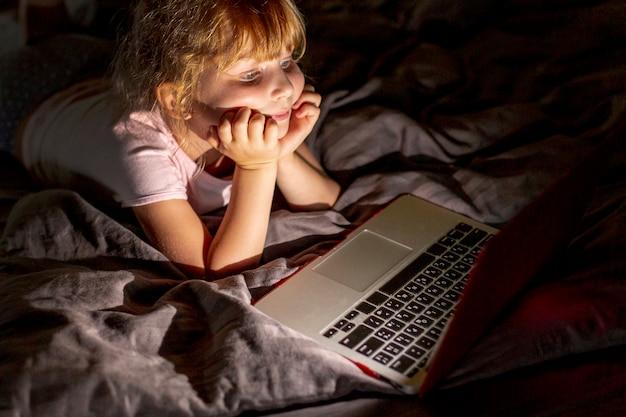 Fille de smiley vue de côté au lit avec un ordinateur portable