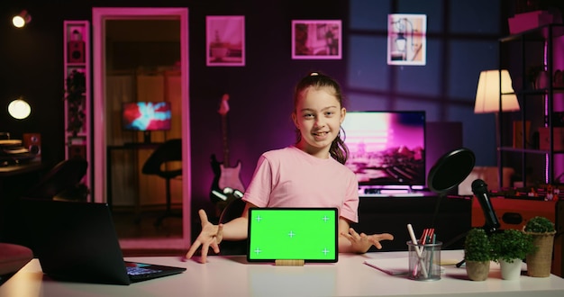 Photo gratuite fille souriante filmant du contenu en ligne avec son parent à l'aide d'une tablette à écran vert du sponsor