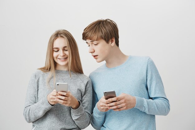 Fille souriante montrant une image mignonne de frère sur téléphone mobile, à la fois à l'aide de smartphones