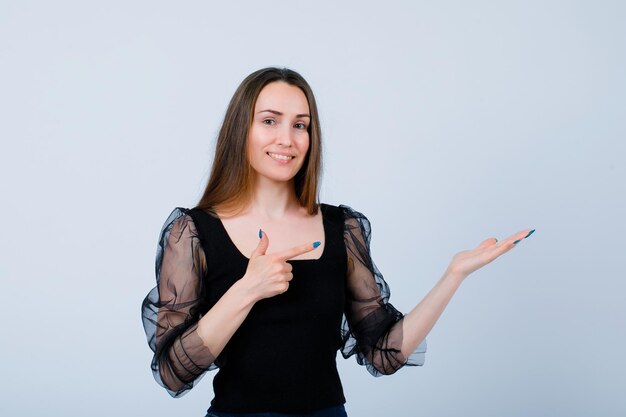 Une fille souriante montre un geste parfait et pointe vers la droite avec la main sur fond blanc