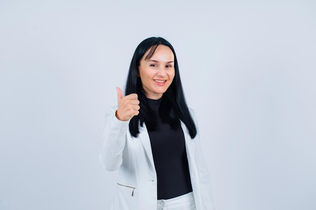 Une fille souriante regarde la caméra en montrant un geste parfait sur fond blanc