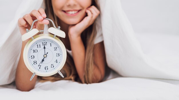 Fille souriante tenant une horloge blanche